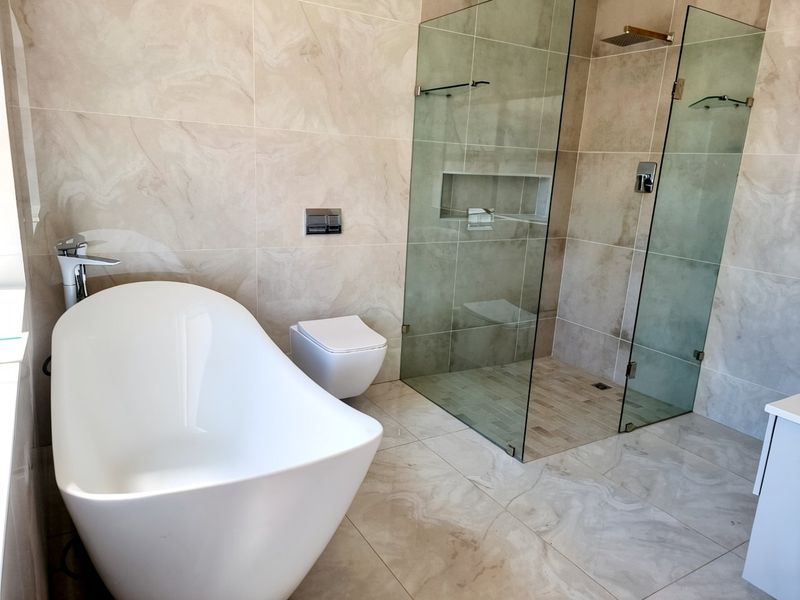Modern bathroom featuring a sleek freestanding bathtub, wall-hung toilet, and a spacious frameless glass walk-in shower with neutral stone-look tiling.