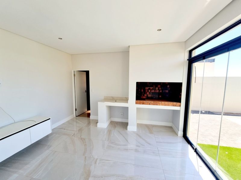 Modern enclosed patio featuring a built-in braai, stone prep area with sink, large format floor tiles, and floor-to-ceiling sliding glass doors.