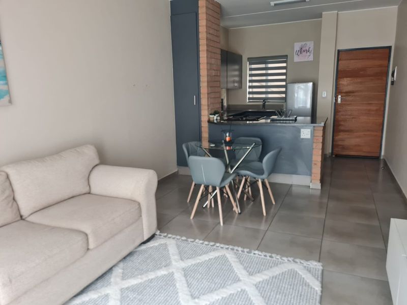Open-plan living and kitchen area featuring tiled floors, an exposed brick feature pillar, and modern cabinetry with integrated kitchen appliances.