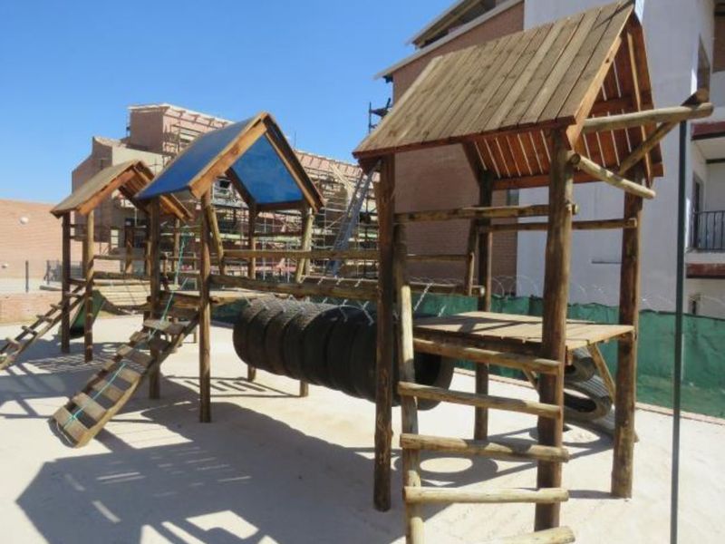 Outdoor wooden playground structure with climbing frames and a tire bridge located within the apartment complex grounds.