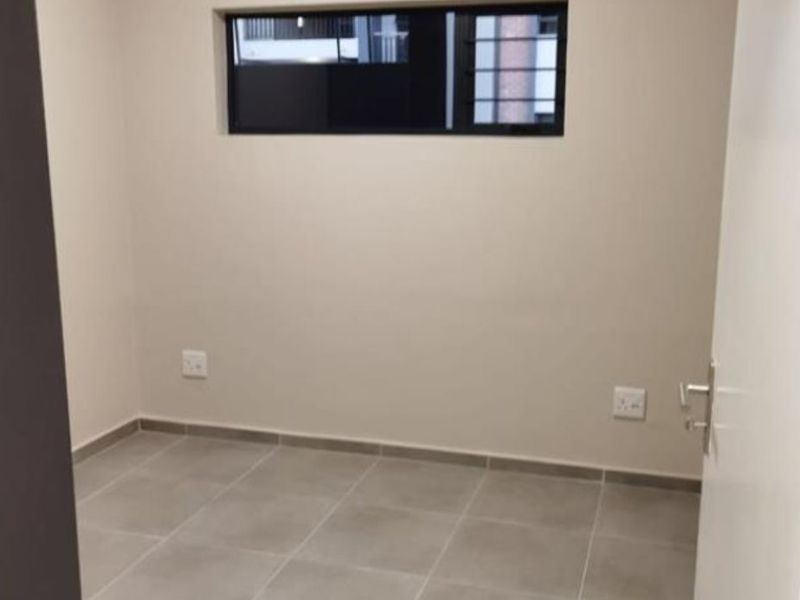 A clean, empty bedroom featuring neutral tiled flooring, a high-level window, and modern electrical outlets, ready for personalization.