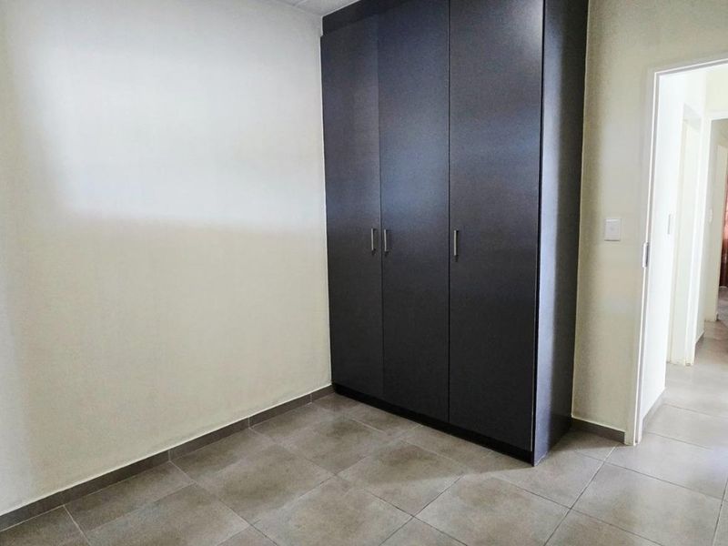 A clean, empty bedroom featuring modern dark built-in cupboards and neutral tiled flooring, offering a versatile space ready for personalization.