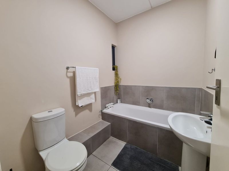 A clean and functional bathroom featuring a built-in bathtub, pedestal basin, and toilet with neutral wall tones and tiled finishes.