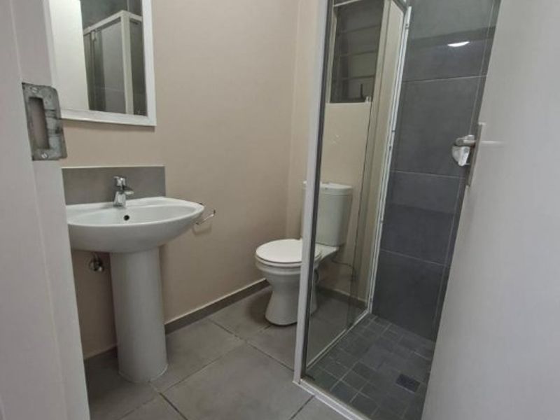 A clean, modern bathroom featuring a pedestal washbasin, a toilet, and a glass-enclosed shower with grey wall tiles.