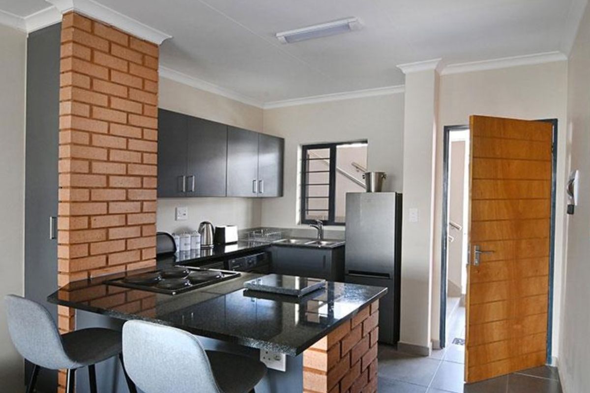Modern kitchen featuring dark cabinetry, granite countertops, a built-in hob, and a distinctive exposed brick pillar, providing a functional and stylish cooking space.