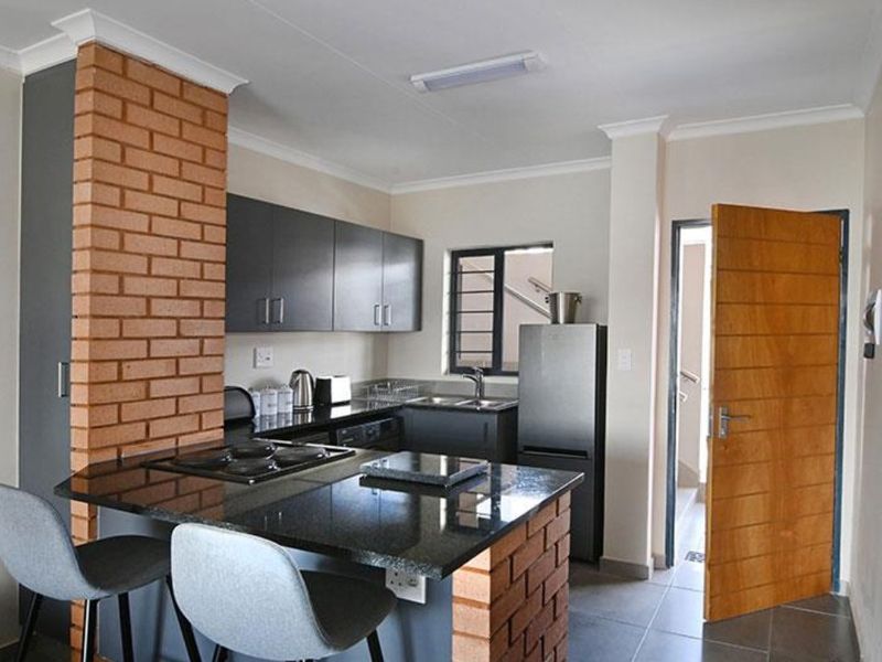 Modern kitchen featuring dark cabinetry, granite countertops, a built-in hob, and a distinctive exposed brick pillar, providing a functional and stylish cooking space.
