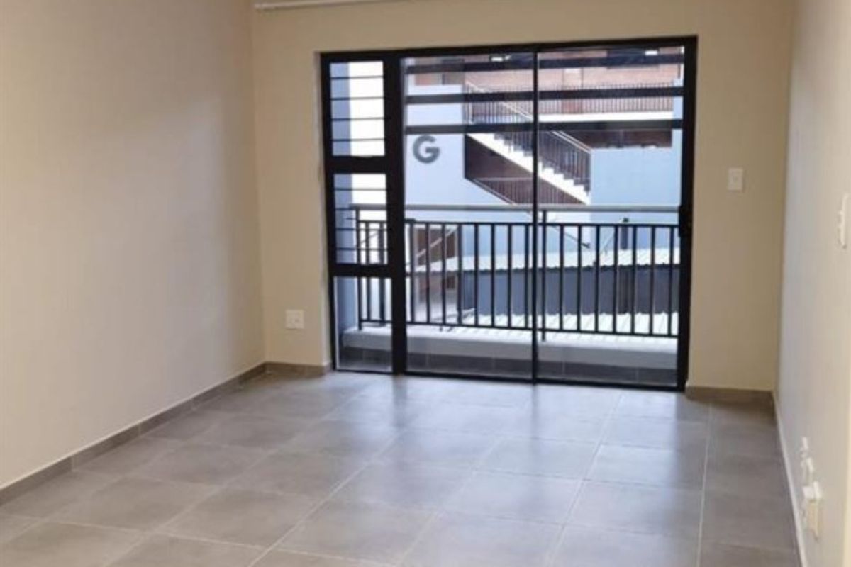 An empty, well-maintained living area featuring neutral tiled flooring and a large sliding glass door with security bars leading to a balcony.