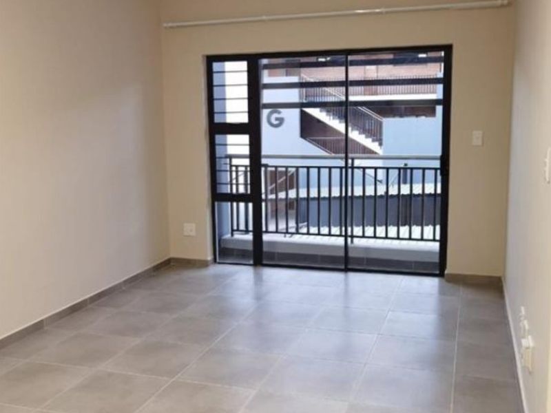 An empty, well-maintained living area featuring neutral tiled flooring and a large sliding glass door with security bars leading to a balcony.