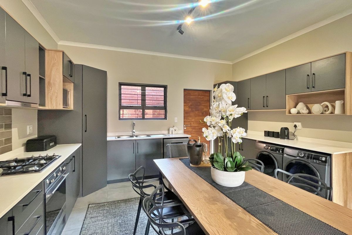 Modern open-plan kitchen featuring sleek grey cabinetry, stone countertops, integrated appliances, and a gas hob, seamlessly flowing into the dining area.