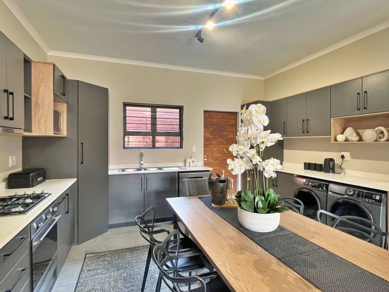 Modern open-plan kitchen featuring sleek grey cabinetry, stone countertops, integrated appliances, and a gas hob, seamlessly flowing into the dining area.