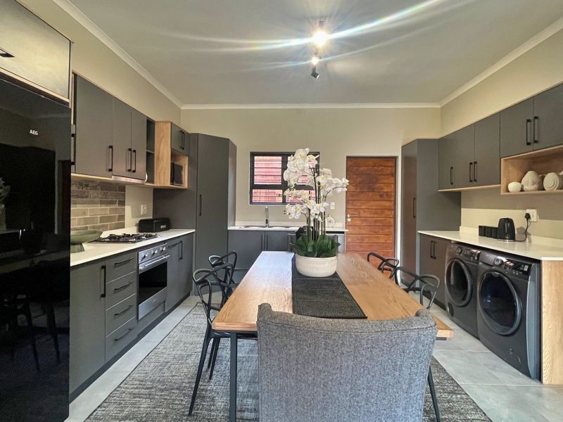 Modern open-plan kitchen and dining area featuring sleek grey cabinetry, wood-tone accents, quartz countertops, and integrated laundry facilities.