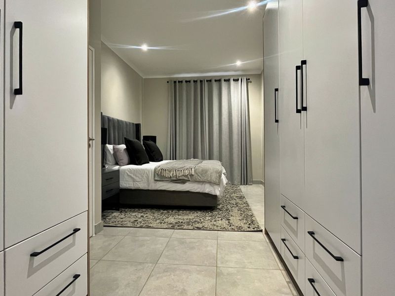 Modern bedroom featuring extensive built-in cupboards, neutral tiled flooring, and recessed downlighting, creating a clean and contemporary living space.