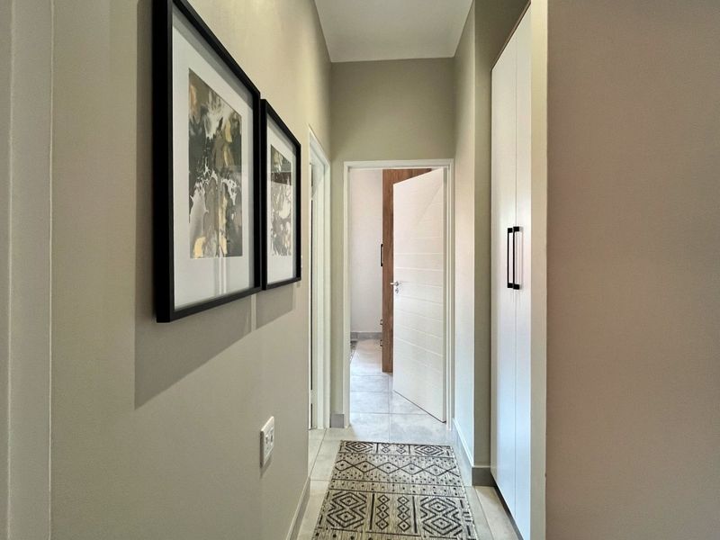 A clean and well-maintained hallway featuring neutral wall tones, tiled flooring, and a built-in storage cupboard.