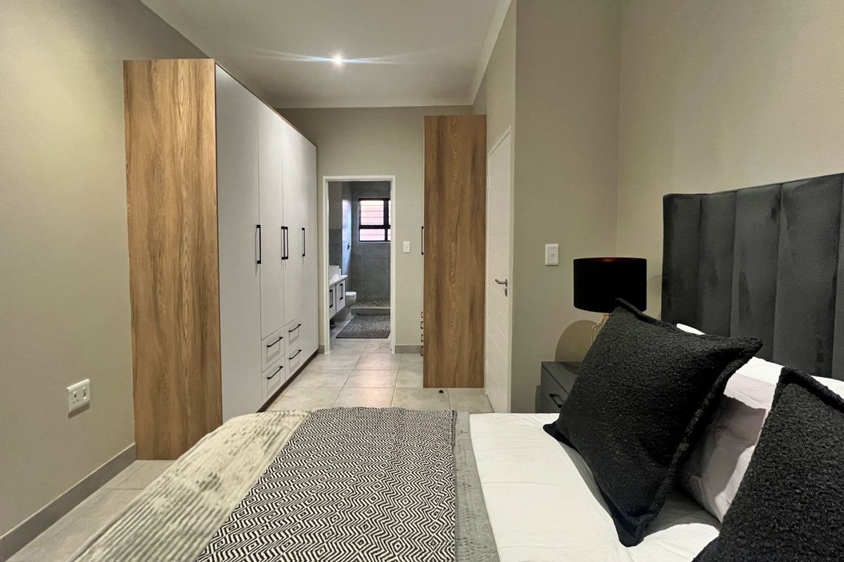A modern bedroom featuring built-in cupboards with wood-grain accents, tiled flooring, recessed lighting, and direct access to an en-suite bathroom.