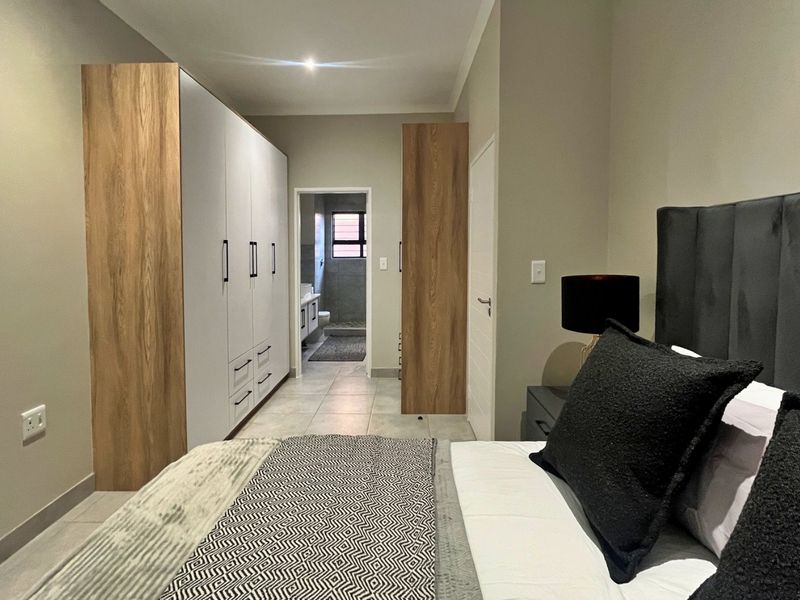 A modern bedroom featuring built-in cupboards with wood-grain accents, tiled flooring, recessed lighting, and direct access to an en-suite bathroom.