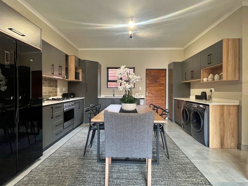 Modern open-plan kitchen and dining area featuring contemporary cabinetry, integrated appliances, and sleek tiled flooring in a well-maintained townhouse setting.