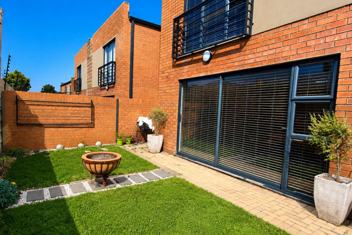 A private rear garden featuring a paved patio area, well-maintained lawn, and face brick exterior with large sliding glass doors.