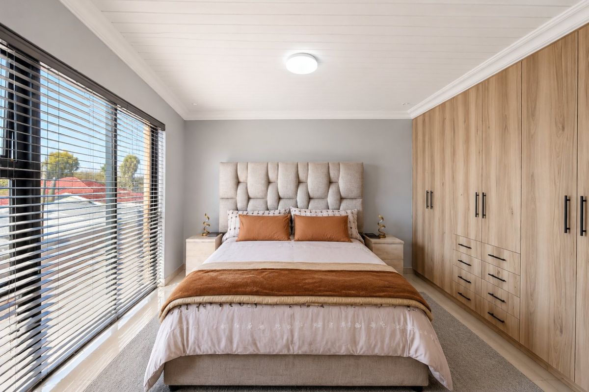A well-maintained bedroom featuring extensive built-in wooden cabinetry, a tongue and groove ceiling, and a large window with venetian blinds.
