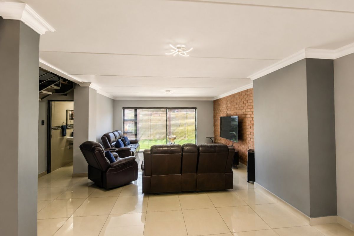 Spacious living room featuring polished tile floors, a prominent exposed brick feature wall, and large sliding glass doors providing natural light and garden access.