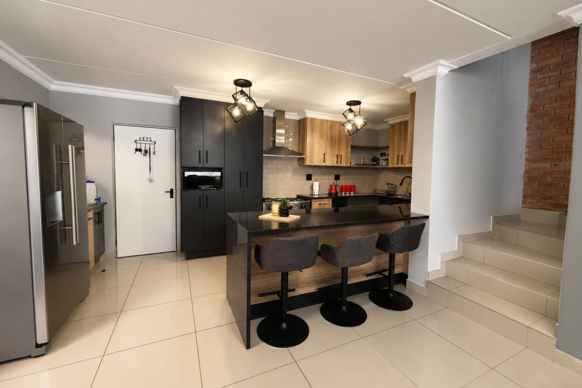 Modern kitchen featuring a central island with granite countertops, sleek cabinetry, integrated appliances, and an adjacent staircase with an exposed brick feature wall.