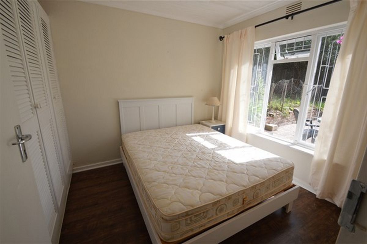 A bedroom featuring built-in louvered cupboards, laminate flooring, and a window with security bars, offering a functional and well-lit living space.