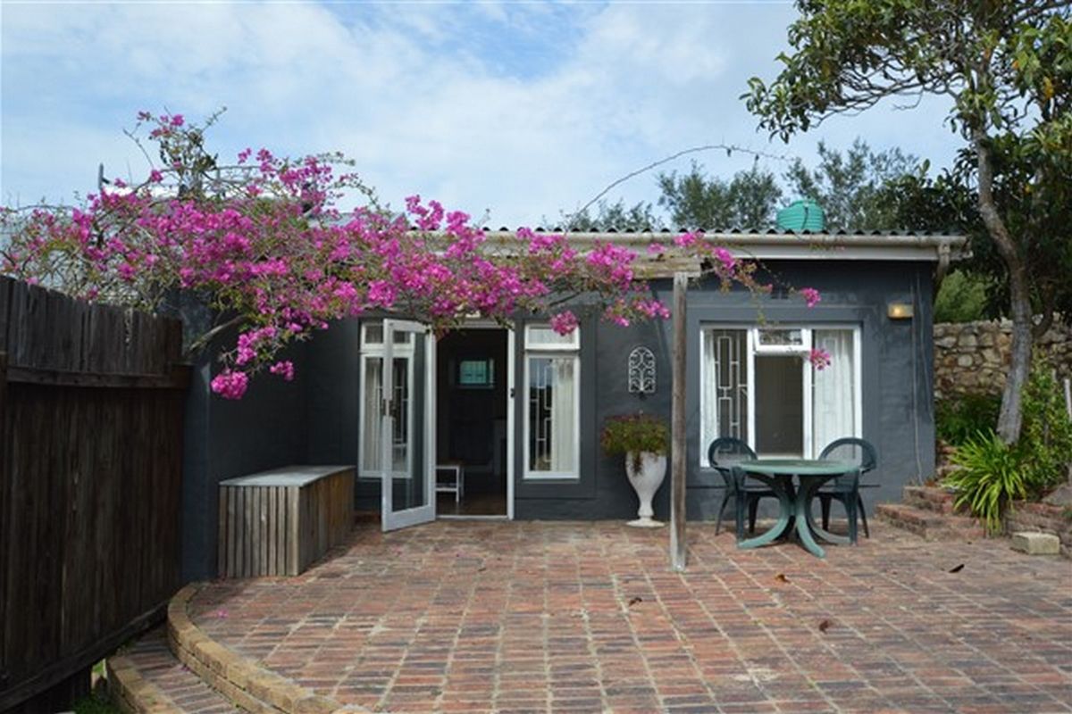 A rear exterior view of the property featuring a brick-paved patio, stone retaining wall, and established garden elements with direct access via french doors.