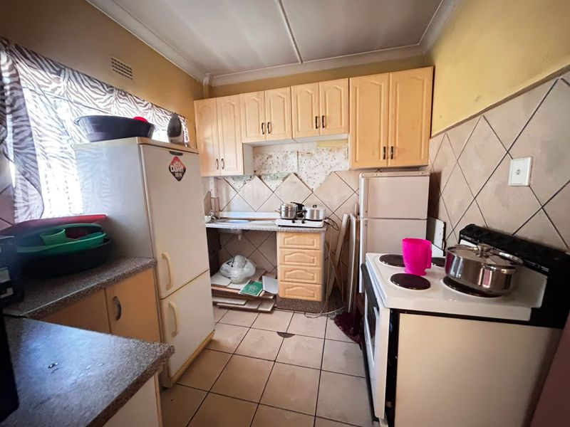 A dated kitchen featuring built-in cabinetry, tiled backsplash, and tiled flooring, currently requiring renovation and cosmetic updates to improve functionality and aesthetic appeal.