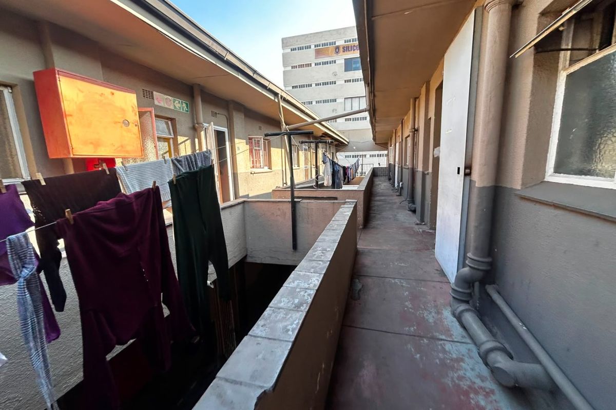 An exterior apartment walkway featuring concrete balustrades and exposed plumbing, showing signs of wear and weathering.