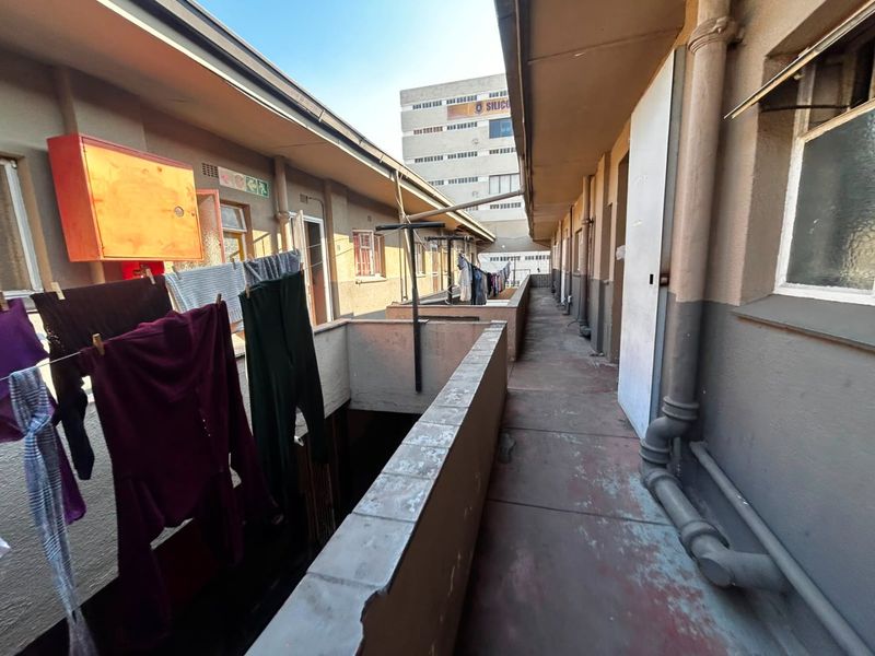 An exterior apartment walkway featuring concrete balustrades and exposed plumbing, showing signs of wear and weathering.