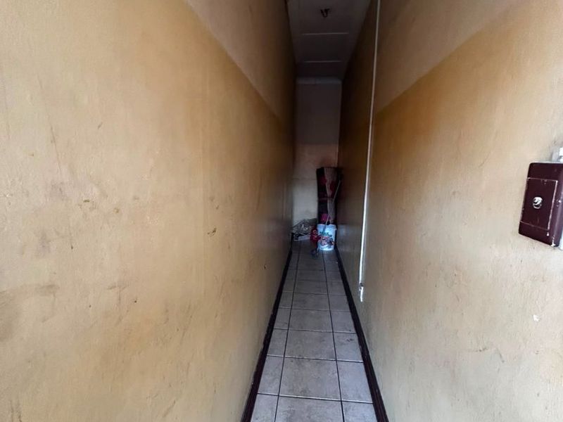 A narrow, vacant hallway featuring tiled flooring and painted walls in need of cosmetic refurbishment and cleaning.