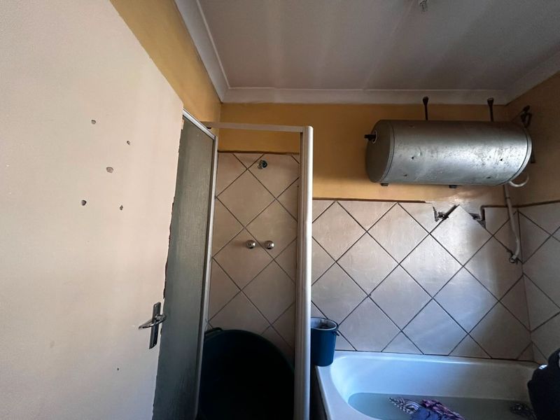 A dated bathroom featuring a shower enclosure, bathtub, and wall-mounted electric water heater, currently requiring significant maintenance and cosmetic updates.