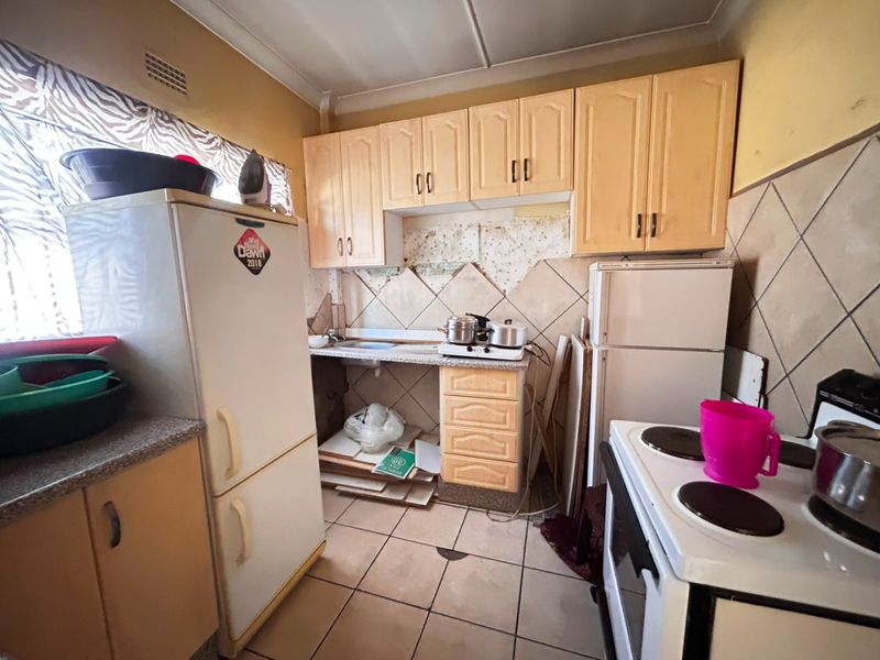 A compact kitchen featuring dated cabinetry, tiled backsplash, and tiled flooring, currently requiring maintenance and cosmetic updates to improve functionality and aesthetic appeal.