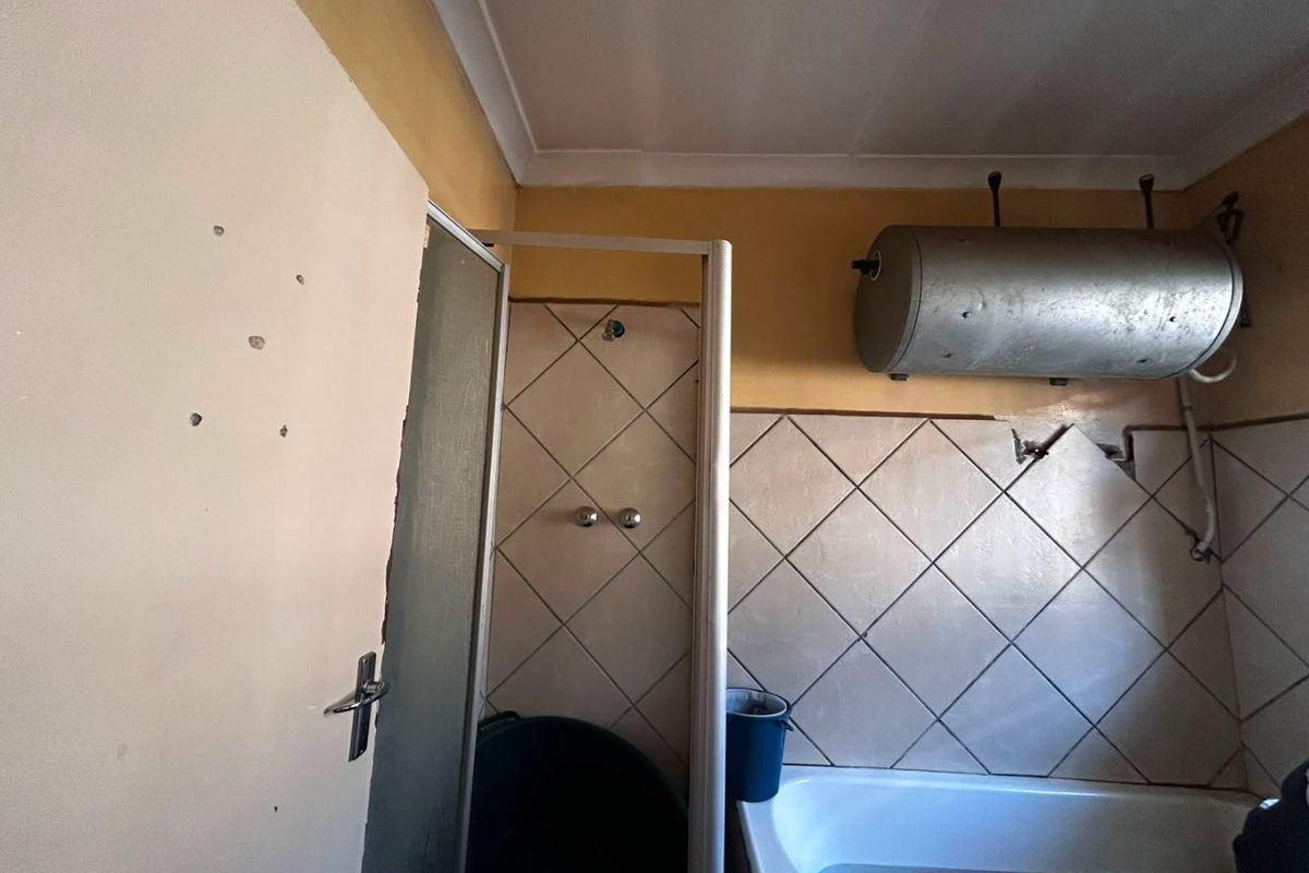 A dated bathroom featuring a shower enclosure, bathtub, and wall-mounted electric water heater, currently requiring significant maintenance and cosmetic updates.