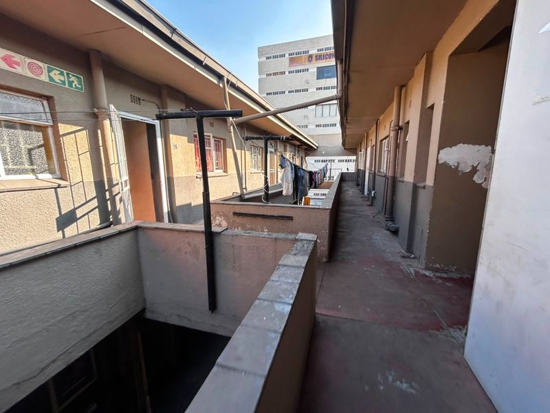 An exterior walkway of an apartment building showing signs of wear, including peeling paint and weathered surfaces, with access to multiple units.