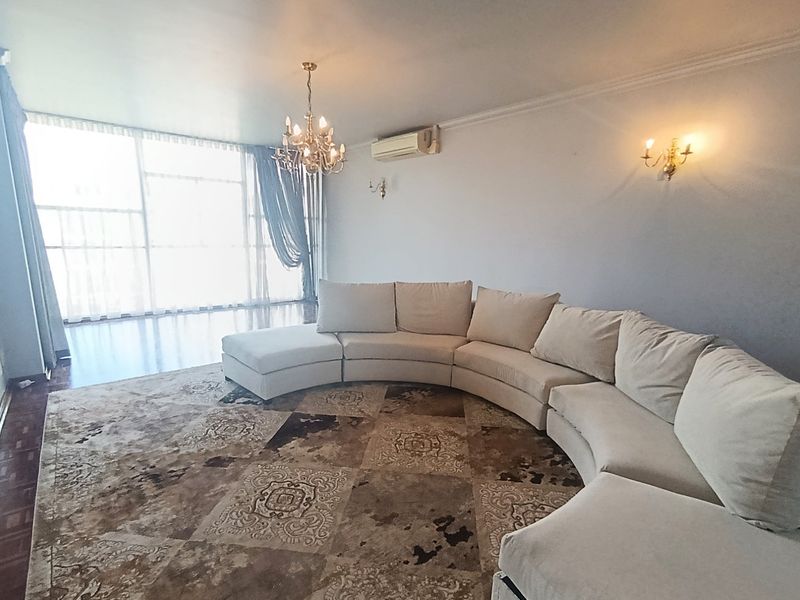Spacious living room featuring large floor-to-ceiling windows, wall-mounted lighting, a central chandelier, and a split-system air conditioning unit.