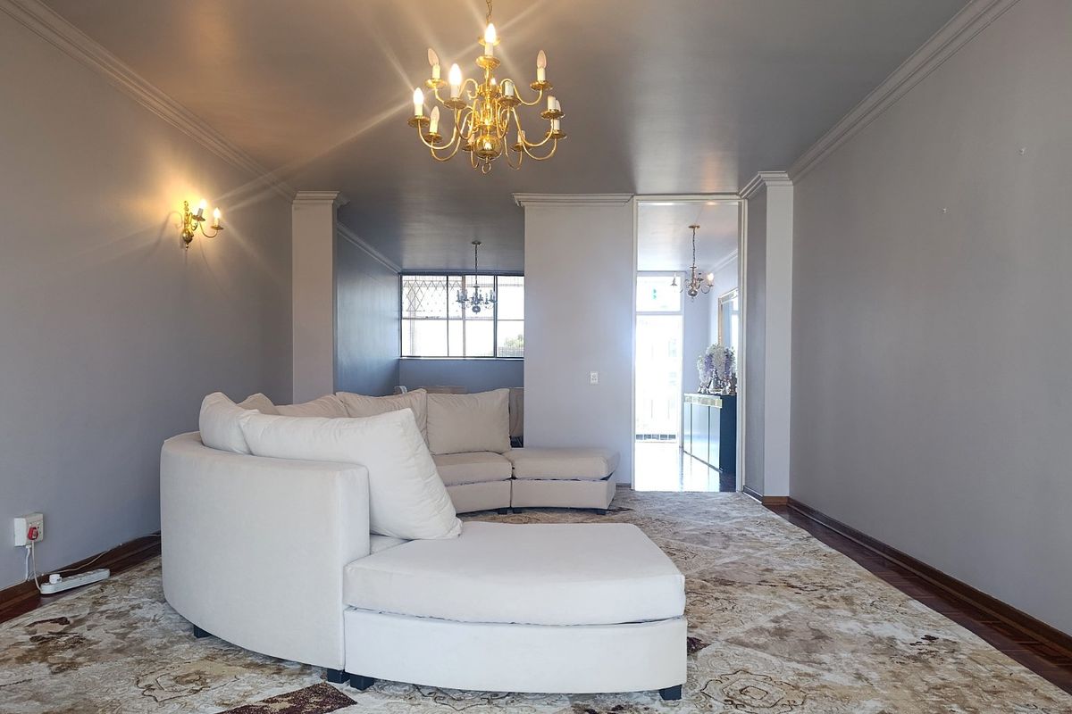 Spacious living room featuring elegant crown molding, classic chandelier lighting, wall sconces, and well-maintained parquet flooring.