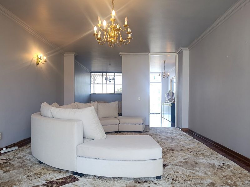 Spacious living room featuring elegant crown molding, classic chandelier lighting, wall sconces, and well-maintained parquet flooring.