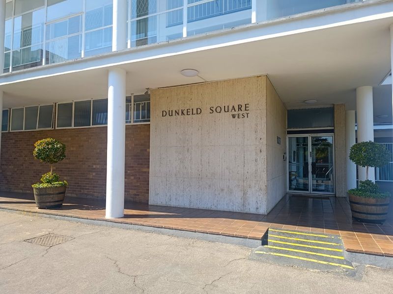 The front entrance of Dunkeld Square West featuring a travertine-clad facade, brickwork, and a glass-panelled main door with a tiled landing.
