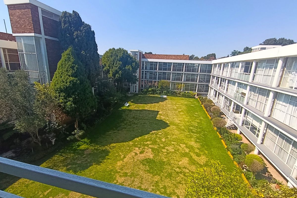 A view overlooking a well-maintained communal garden area surrounded by multi-story apartment blocks with large windows and balcony access.