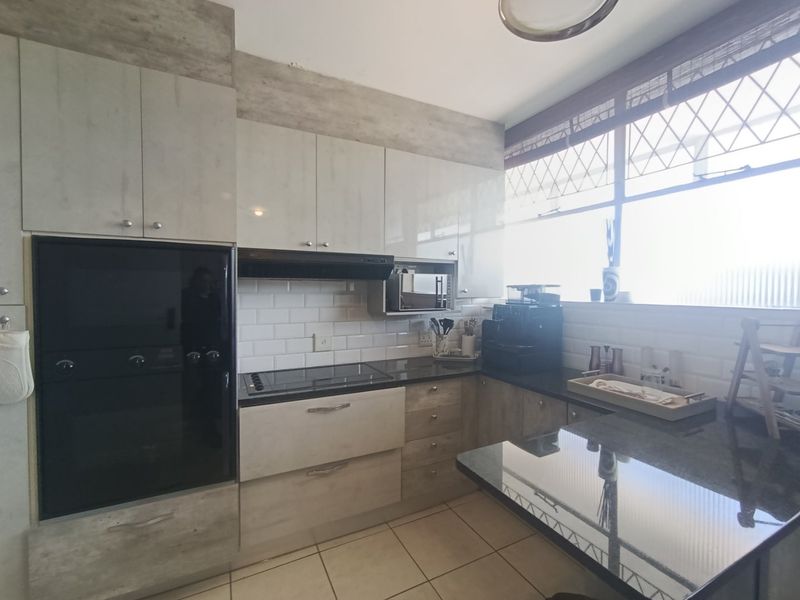 Modern kitchen featuring sleek laminate cabinetry, granite countertops, subway tile backsplash, and integrated appliances including an oven, hob, and microwave.