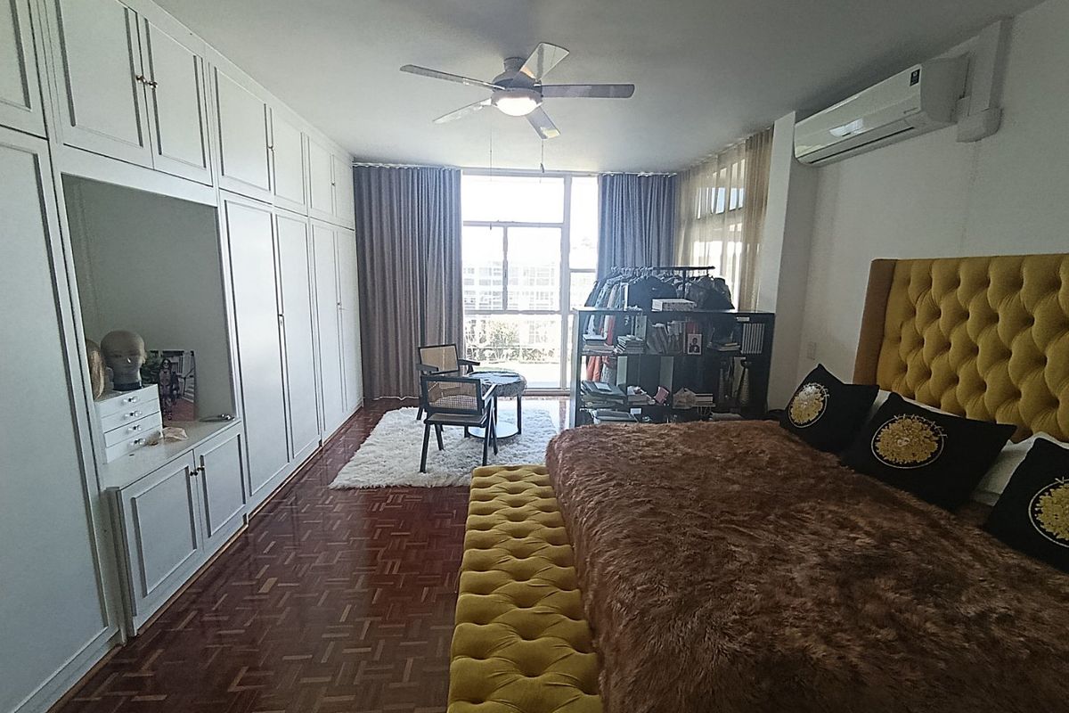 Spacious bedroom featuring extensive built-in cabinetry, parquet flooring, a ceiling fan, and a wall-mounted air conditioning unit.