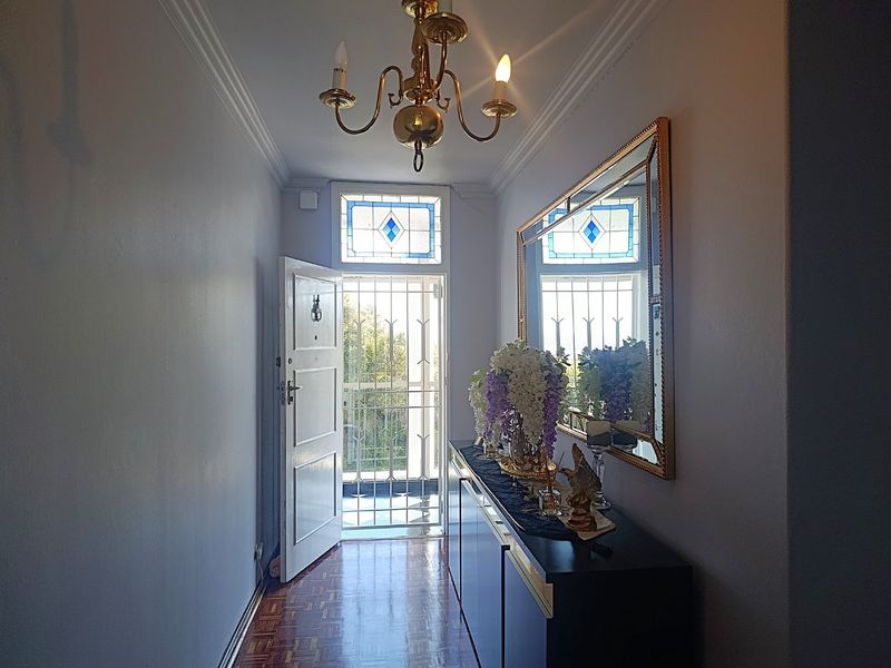 Welcoming entrance hall featuring classic parquet flooring, ornate ceiling cornicing, a brass chandelier, and a decorative stained glass transom window above the security door.