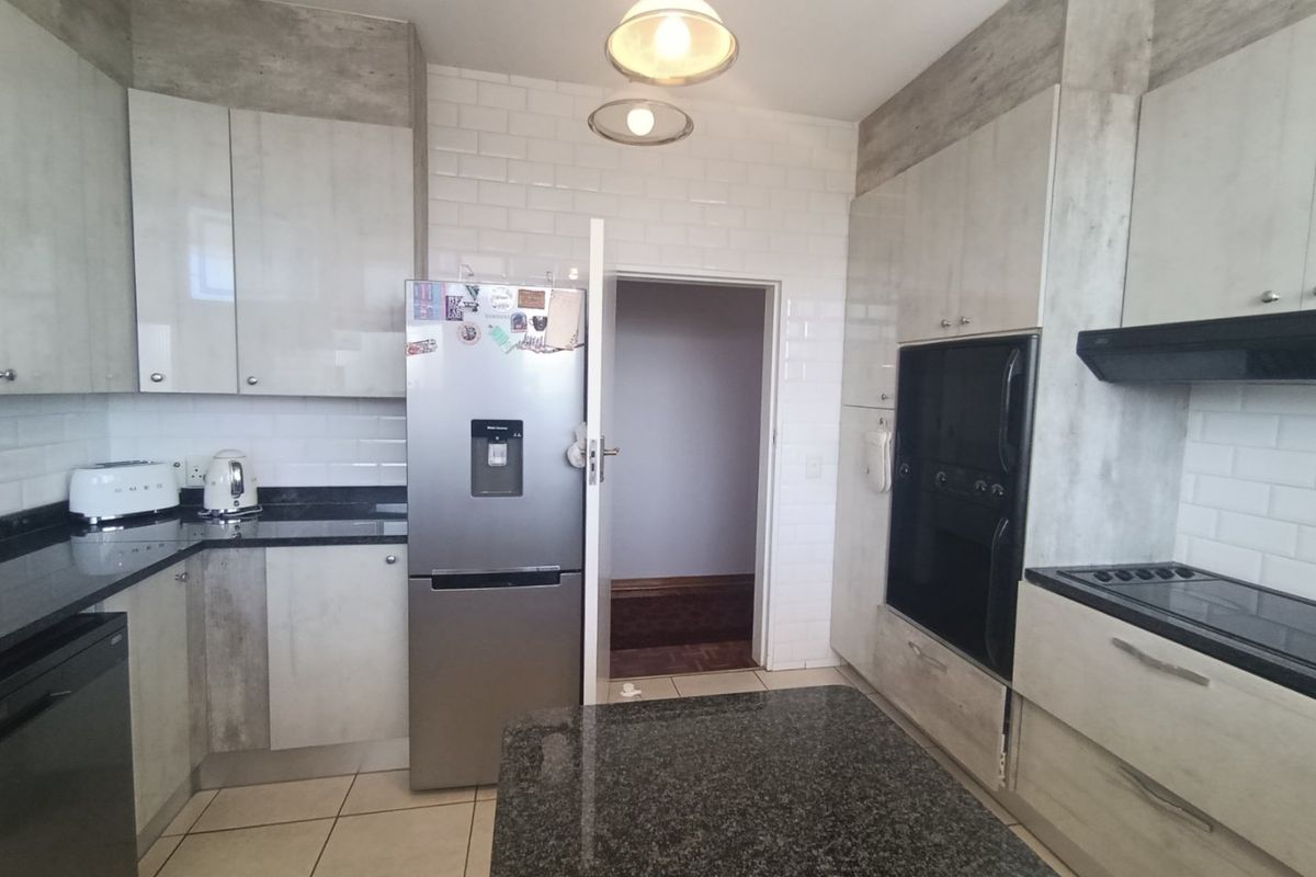 Modern kitchen featuring granite countertops, subway tile backsplash, built-in oven, electric hob, and ample cabinetry for storage.