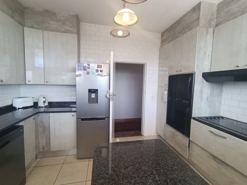 Modern kitchen featuring granite countertops, subway tile backsplash, built-in oven, electric hob, and ample cabinetry for storage.