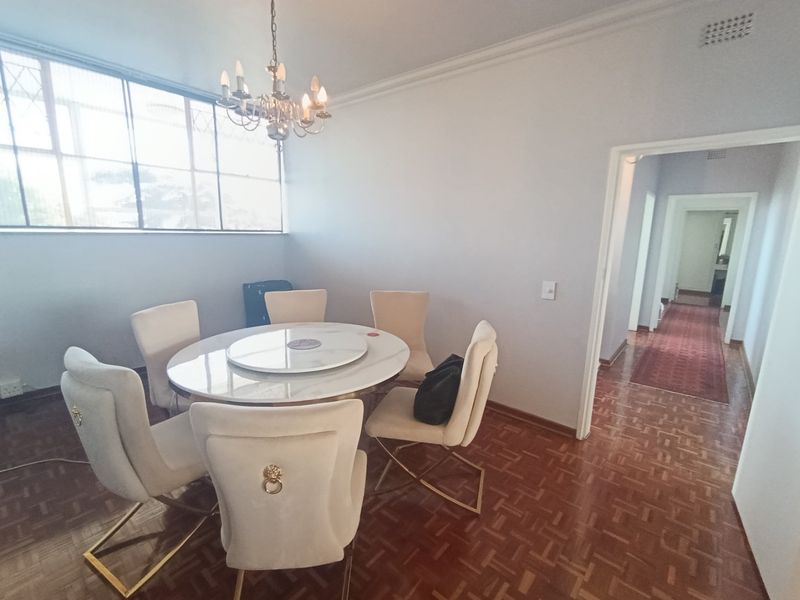 A dining room featuring classic parquet flooring, a decorative chandelier, and large metal-framed windows, leading into a hallway.