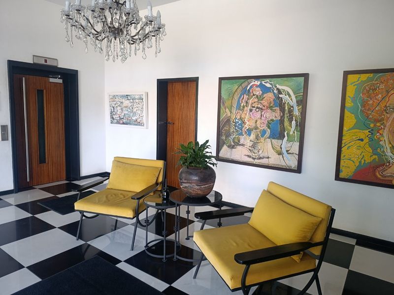 A well-maintained apartment building entrance lobby featuring a classic black and white checkered floor, elegant crystal chandelier, and secure elevator access.