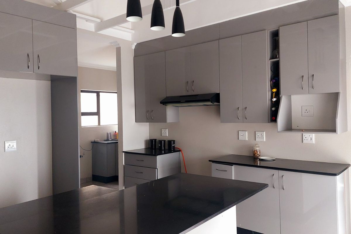 Modern kitchen featuring sleek grey cabinetry, contrasting black granite countertops, integrated wine storage, and contemporary pendant lighting.