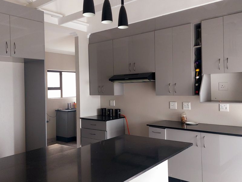 Modern kitchen featuring sleek grey cabinetry, contrasting black granite countertops, integrated wine storage, and contemporary pendant lighting.