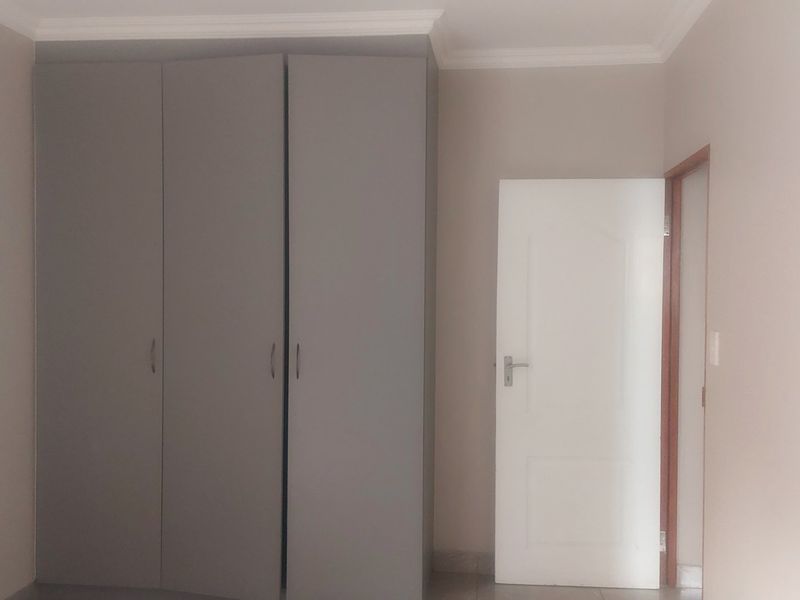 A clean, empty bedroom featuring neutral wall tones, built-in grey cupboards, and classic coving detail.