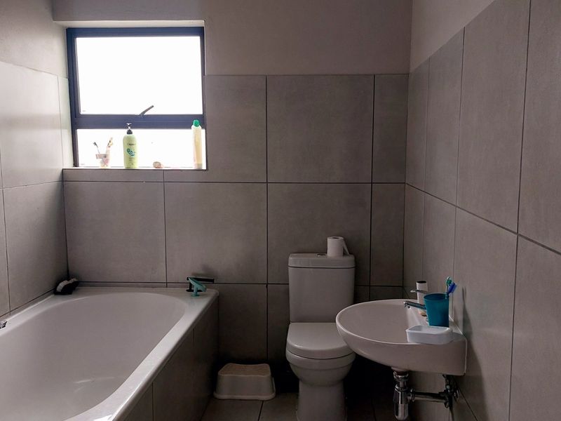 A functional bathroom featuring a bathtub, pedestal basin, and toilet with neutral wall and floor tiling.